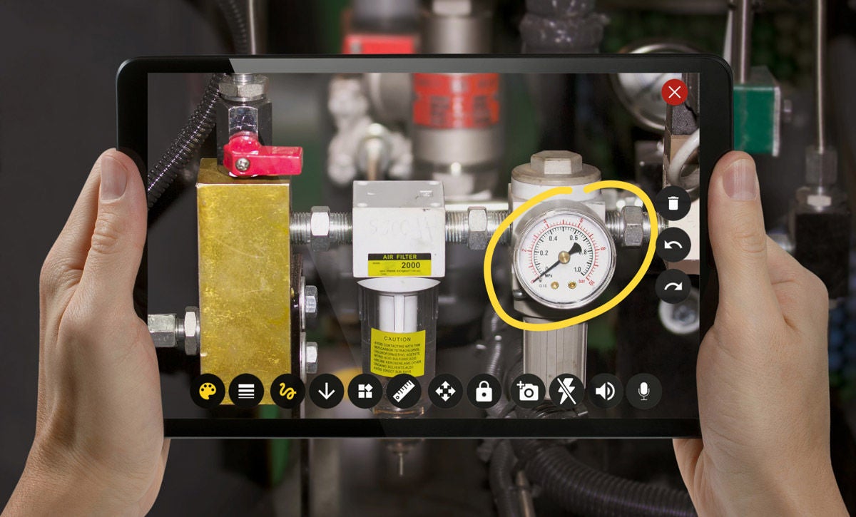 Image of person holding tablet, using table to scan machinery for remote fixes.